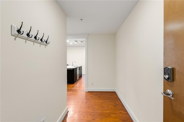 corridor featuring a sink, light wood-type flooring, and baseboards