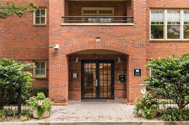 entrance to property featuring brick siding, french doors, and a balcony