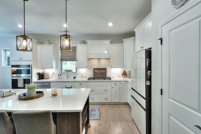 kitchen featuring light wood-style flooring, a sink, appliances with stainless steel finishes, backsplash, and custom range hood