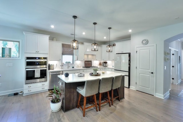 kitchen with arched walkways, white cabinets, a center island, stainless steel appliances, and light countertops