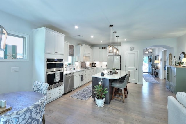 kitchen featuring white cabinets, appliances with stainless steel finishes, arched walkways, and a wealth of natural light