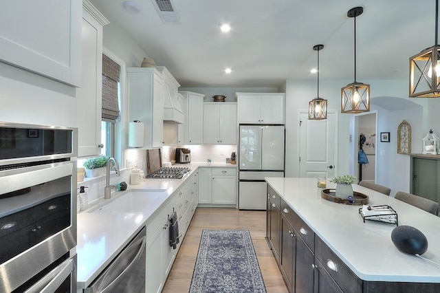 kitchen featuring stainless steel appliances, a sink, visible vents, white cabinetry, and a center island