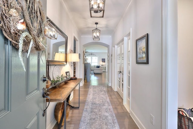 interior space with arched walkways, baseboards, wood finished floors, and crown molding