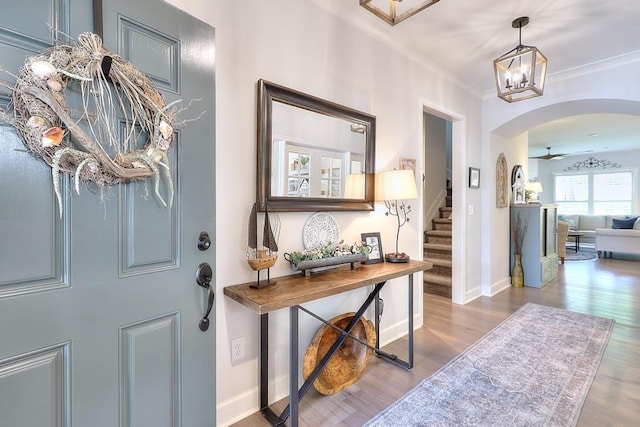 entryway featuring crown molding, stairway, arched walkways, and wood finished floors