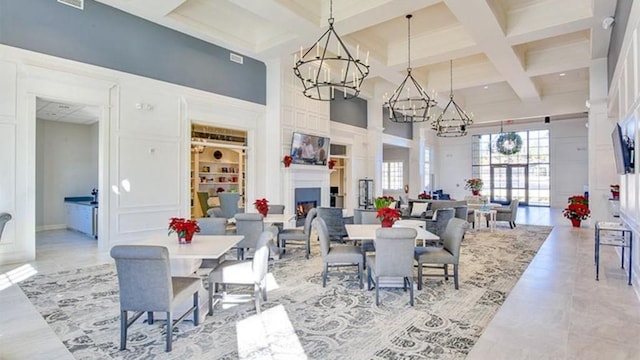 dining space featuring a towering ceiling, an inviting chandelier, coffered ceiling, beamed ceiling, and a lit fireplace