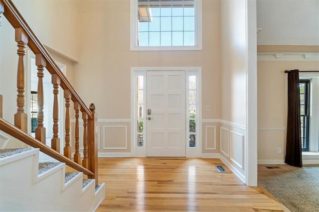 entryway featuring a decorative wall, a high ceiling, light wood finished floors, and wainscoting