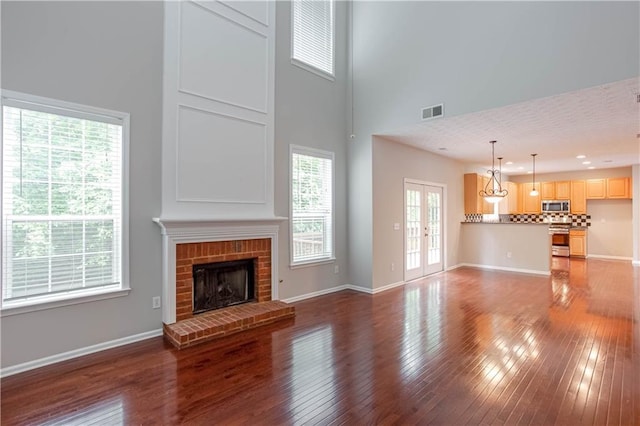 unfurnished living room with a high ceiling, a fireplace, hardwood / wood-style flooring, and french doors