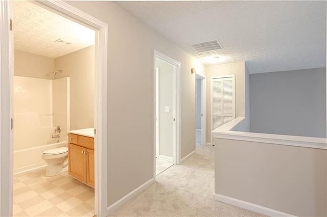 corridor featuring a textured ceiling and light colored carpet