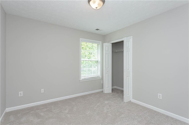 unfurnished bedroom featuring a textured ceiling, light colored carpet, and a closet