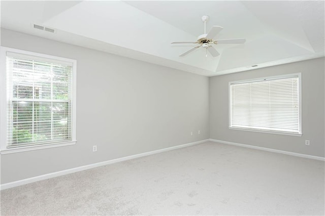 carpeted spare room with a raised ceiling, ceiling fan, and a wealth of natural light