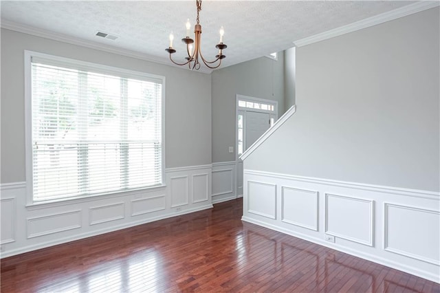 empty room with a textured ceiling, a notable chandelier, dark hardwood / wood-style floors, and crown molding