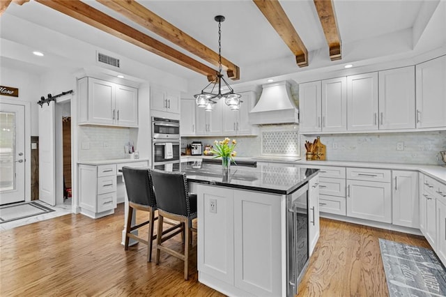 415 Southridge Rd, Winder, GA 30680 - kitchen featuring custom exhaust hood, light wood-type flooring, stainless steel double oven, white cabinetry, and beamed ceiling