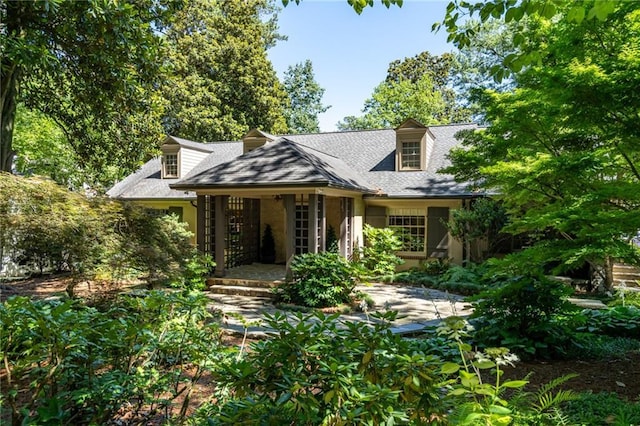 cape cod home featuring a shingled roof and covered porch