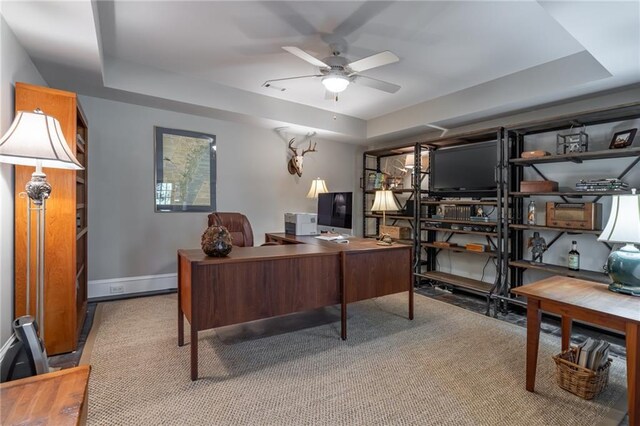 home office featuring a ceiling fan, a raised ceiling, and baseboards