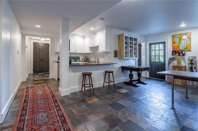 kitchen featuring stone tile floors, recessed lighting, baseboards, white cabinets, and a kitchen bar