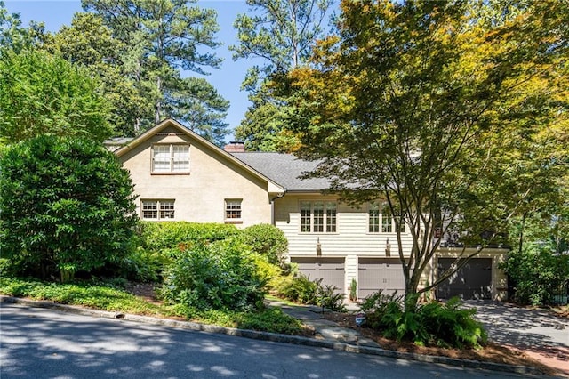 view of front of home with concrete driveway, a chimney, an attached garage, and stucco siding