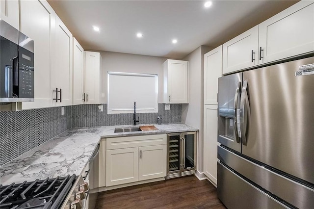 kitchen with light stone countertops, dark wood-style flooring, a sink, white cabinets, and appliances with stainless steel finishes