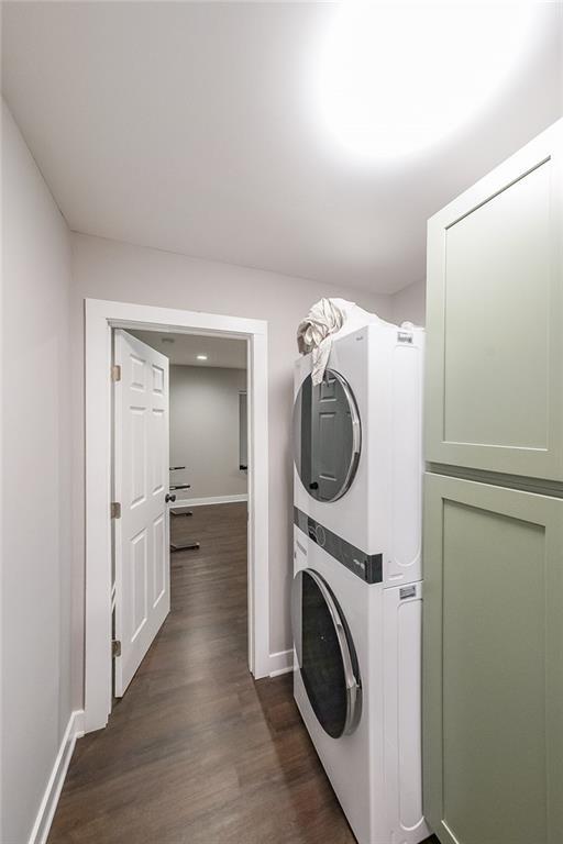 washroom featuring dark wood finished floors, laundry area, baseboards, and stacked washing maching and dryer