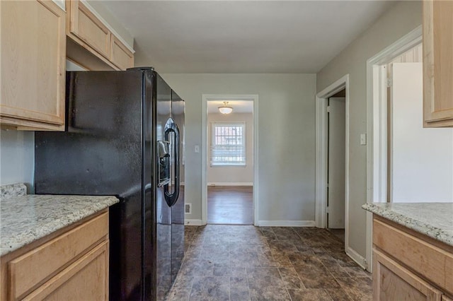 kitchen with light stone countertops, light brown cabinetry, and black refrigerator with ice dispenser