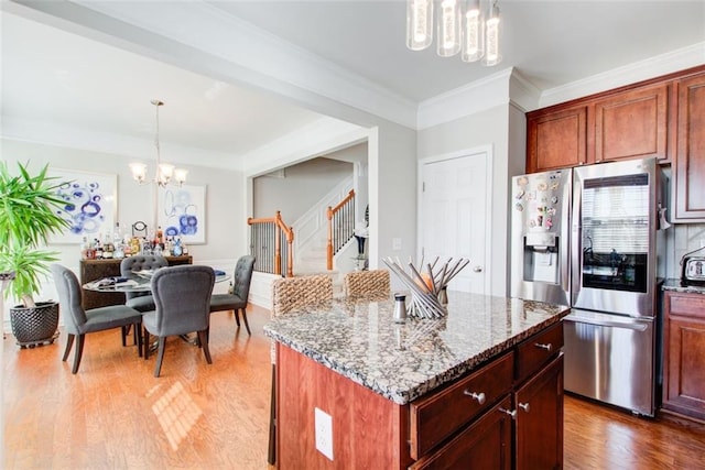 kitchen with light stone counters, a chandelier, stainless steel fridge, a kitchen island, and pendant lighting