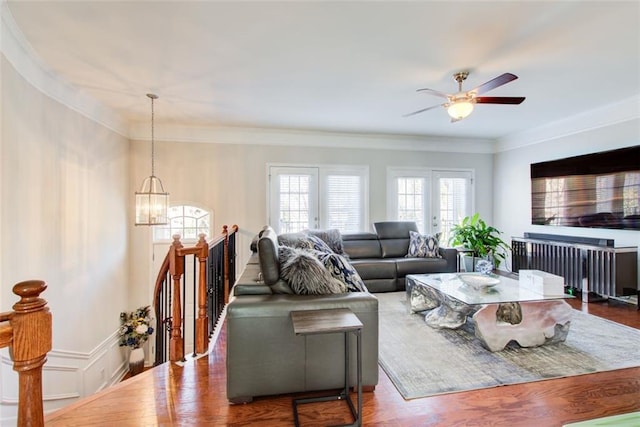 living room with crown molding, wood-type flooring, ceiling fan with notable chandelier, and french doors