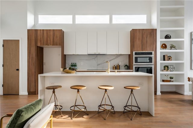 kitchen with white cabinets, a kitchen bar, stainless steel double oven, and sink