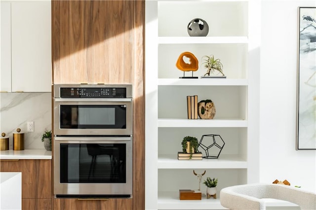 kitchen with white cabinets, built in shelves, double oven, and tasteful backsplash