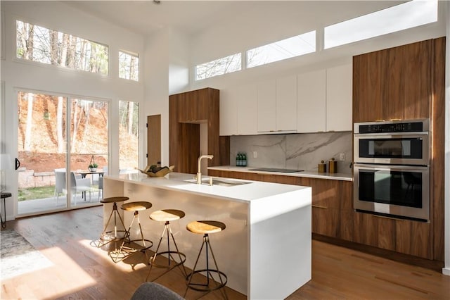 kitchen with double oven, sink, white cabinets, tasteful backsplash, and a kitchen bar