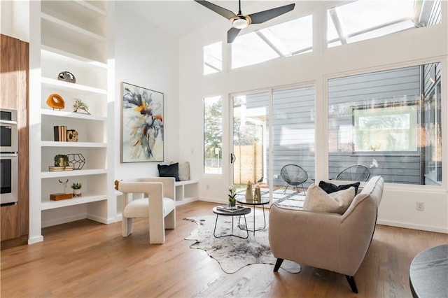 sitting room with light wood-type flooring, built in shelves, and ceiling fan