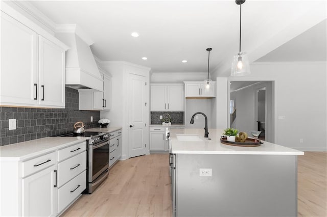 kitchen featuring light wood-type flooring, stainless steel range with electric stovetop, sink, white cabinets, and an island with sink