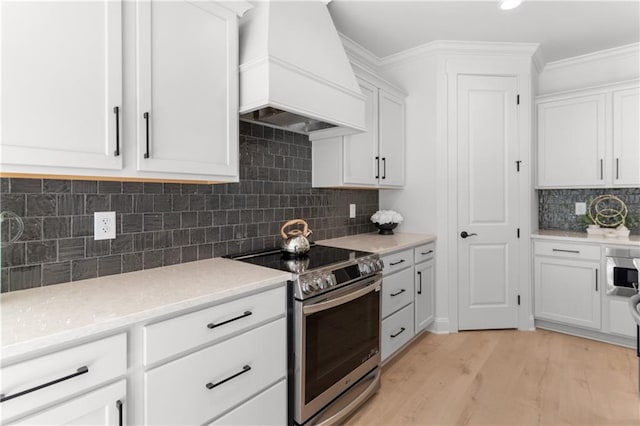 kitchen featuring white cabinets, light hardwood / wood-style flooring, stainless steel electric range oven, tasteful backsplash, and custom range hood