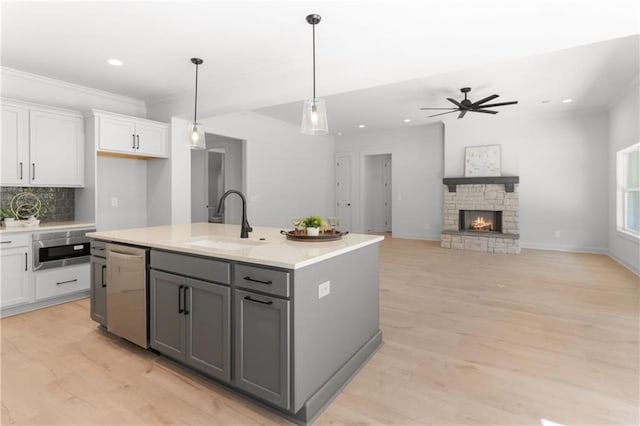 kitchen featuring stainless steel dishwasher, ceiling fan, sink, white cabinets, and an island with sink