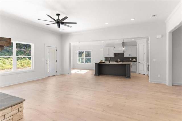 kitchen featuring light wood-type flooring, hanging light fixtures, ornamental molding, and a kitchen island with sink