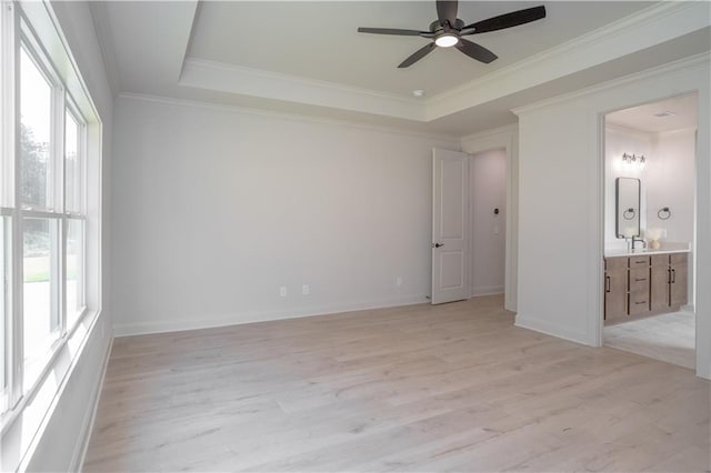 unfurnished bedroom featuring connected bathroom, ceiling fan, light hardwood / wood-style flooring, a tray ceiling, and ornamental molding