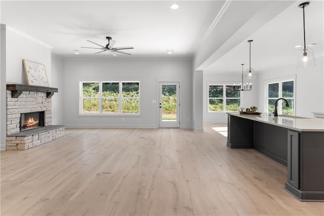 unfurnished living room with sink, crown molding, light hardwood / wood-style floors, a fireplace, and ceiling fan with notable chandelier