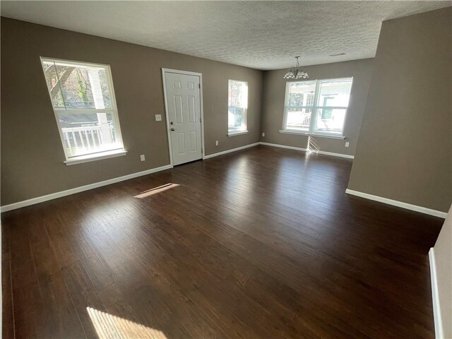 spare room with an inviting chandelier, baseboards, dark wood-type flooring, and a wealth of natural light