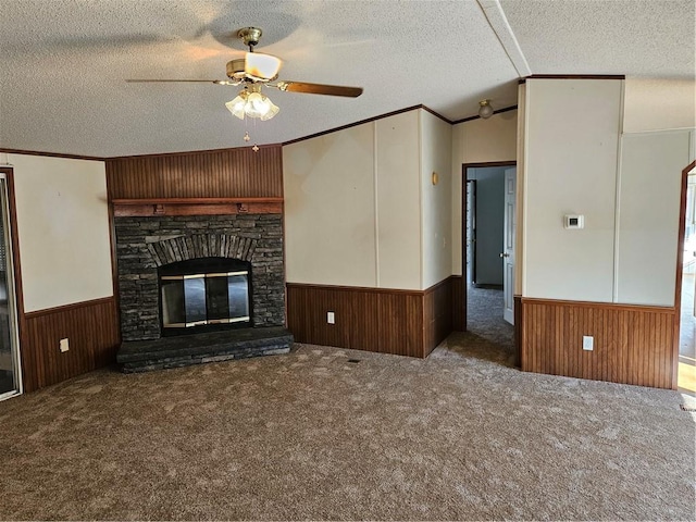 unfurnished living room with dark colored carpet, a stone fireplace, ceiling fan, and ornamental molding