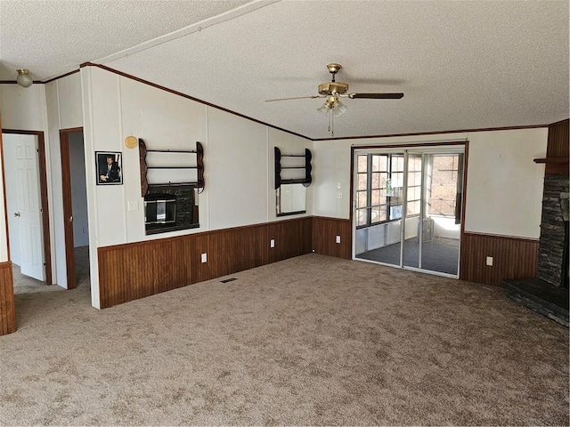 unfurnished living room with ceiling fan, a stone fireplace, carpet floors, a textured ceiling, and ornamental molding