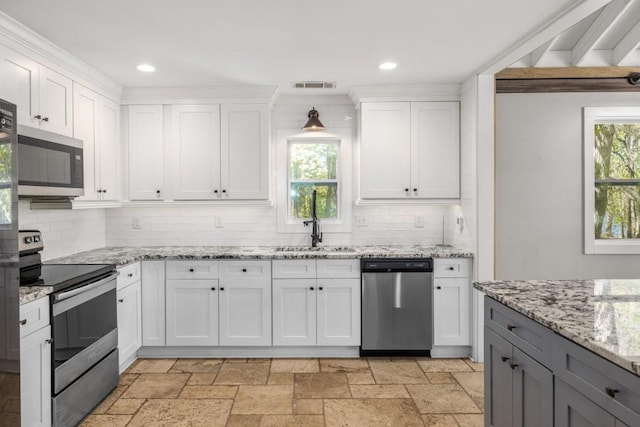 kitchen featuring stainless steel appliances, a sink, backsplash, white cabinetry, and stone tile floors