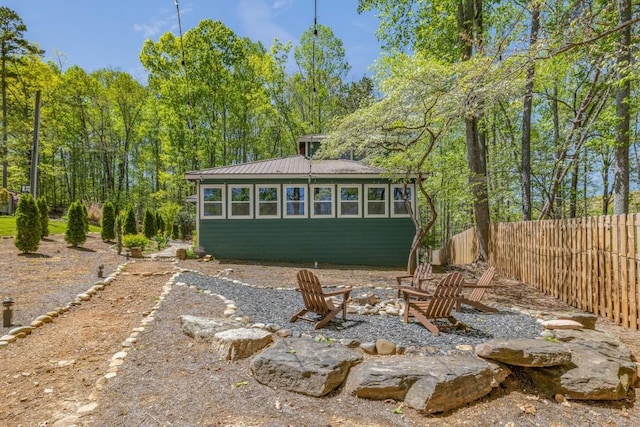 back of house with fence, an outdoor fire pit, metal roof, and an outbuilding