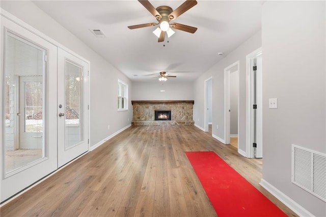 unfurnished living room featuring french doors, ceiling fan, a stone fireplace, and light hardwood / wood-style flooring