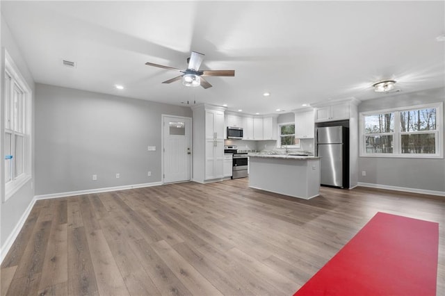 kitchen featuring light hardwood / wood-style flooring, appliances with stainless steel finishes, light stone counters, white cabinets, and a kitchen island