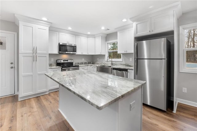 kitchen with appliances with stainless steel finishes, light stone countertops, a kitchen island, and white cabinets