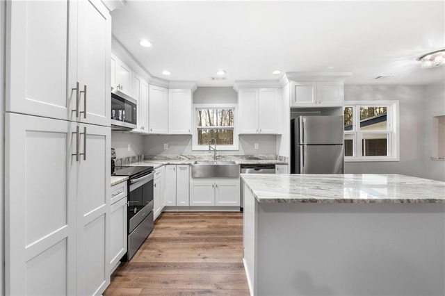 kitchen with white cabinetry, stainless steel appliances, light stone countertops, and sink