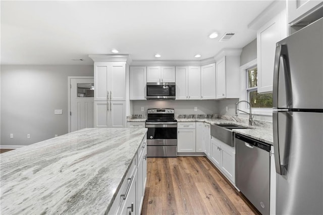 kitchen featuring appliances with stainless steel finishes, sink, white cabinets, dark hardwood / wood-style flooring, and light stone counters