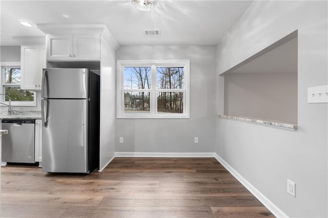 kitchen featuring stainless steel appliances, light stone countertops, wood-type flooring, and white cabinets