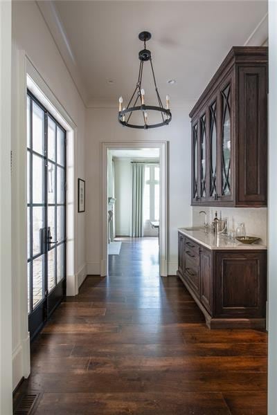 interior space with pendant lighting, dark wood-type flooring, dark brown cabinetry, an inviting chandelier, and sink