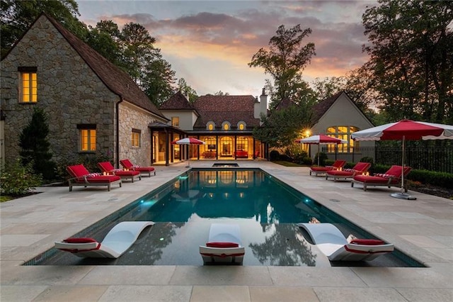 pool at dusk with an outdoor living space and a patio area