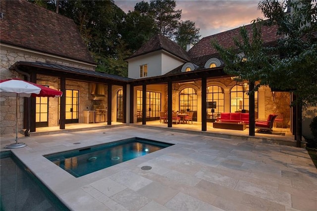 back house at dusk featuring a patio and an in ground hot tub