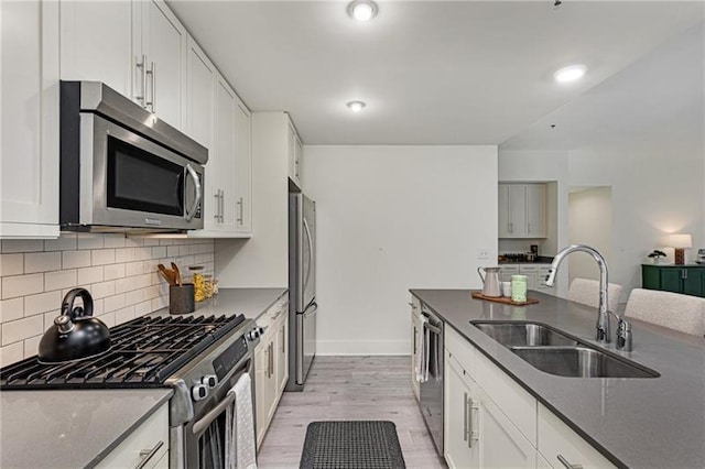 kitchen featuring sink, white cabinetry, tasteful backsplash, light wood-type flooring, and appliances with stainless steel finishes